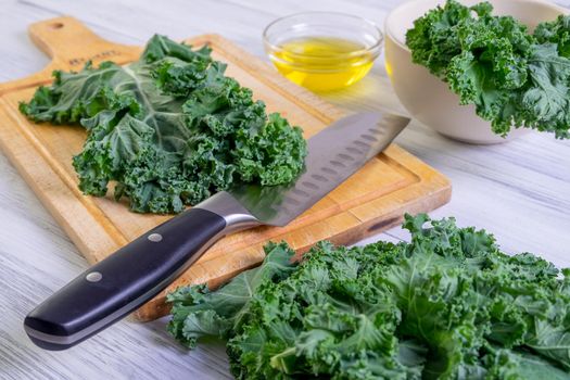 Kale leaves in a large kitchen knife on a wooden cutting board. Super food concept, healthy and vegetarian food. Selective focus.