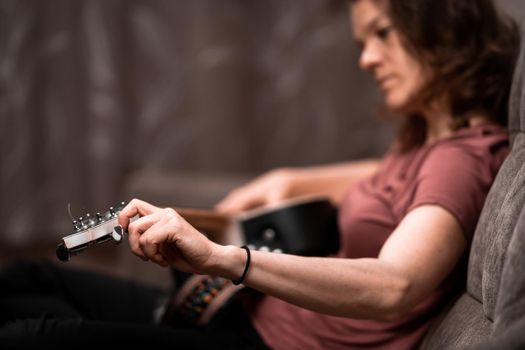 woman tuning guitar at home on the couch.