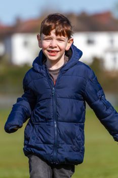 A cute, blue-eyed, redhead boy wearing a blue jacket running on a park on a sunny spring day