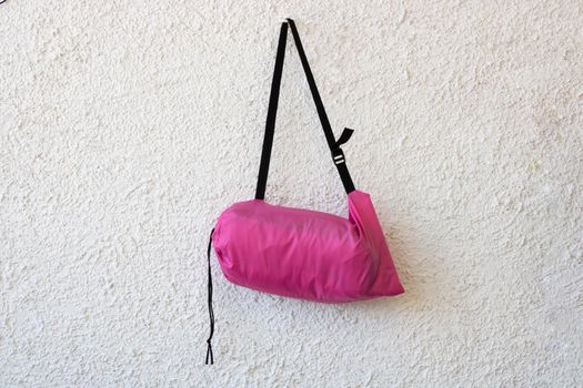 Pink sports bag with a black belt on a white rough background.