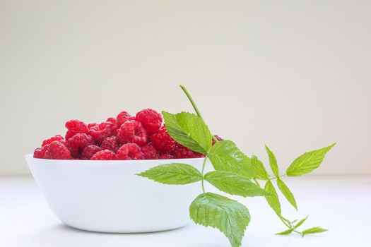 Big Pile of Fresh Raspberries and leaf in transparent bowl on the white background