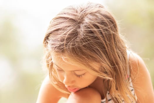 Little blonde girl with head bowed, looking down