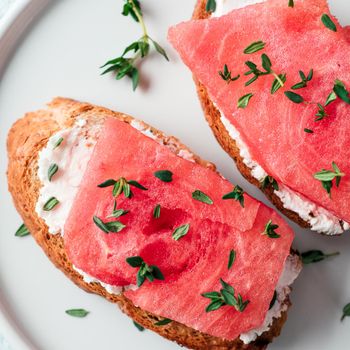 Toasts with soft cheese and watermelon.Salty cheese,sweet watermelon and spicy thyme on crispy grilled bread slices.Idea and recipe unusual healthy breakfast,summer snack.Top view,flat lay. Copy space