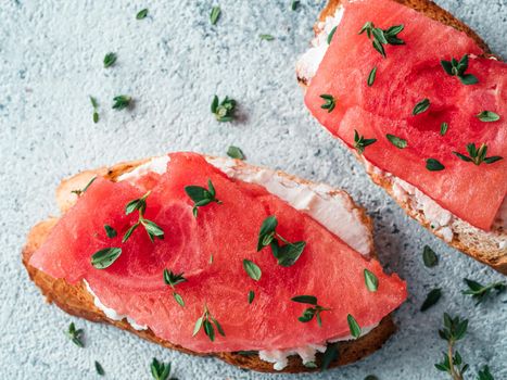 Toasts with soft cheese and watermelon.Salty cheese,sweet watermelon and spicy thyme on crispy grilled bread slices.Idea and recipe unusual healthy breakfast,summer snack.Top view,flat lay. Copy space