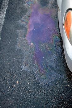 Colorful gas stain on wet asphalt. Oil stain caused by a leak under a car. Environmental pollution concept.