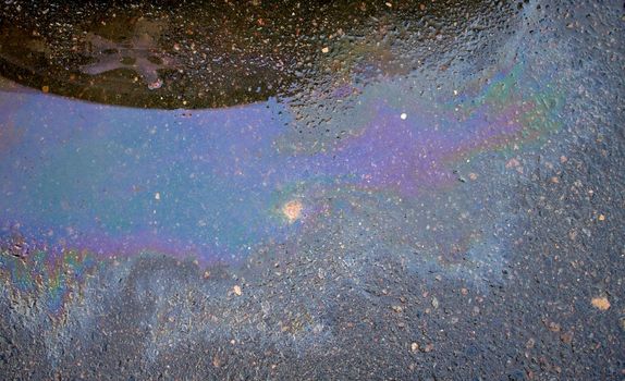 Colorful gas stain on wet asphalt. Oil stain caused by a leak under a car. Environmental pollution concept.