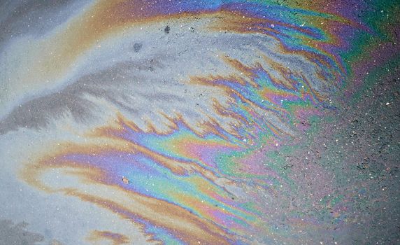 Gasoline flows on the asphalt surface. Iridescent stains of gasoline.