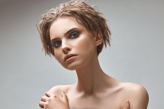 Portrait of a charming young woman with bare shoulders on a gray background in the studio.