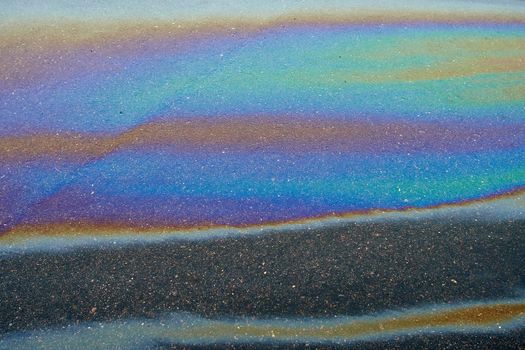 Abstract rainbow effect, colorful gas stain on wet asphalt.Rainbow gasoline leak after a car on a pedestrian sidewalk.