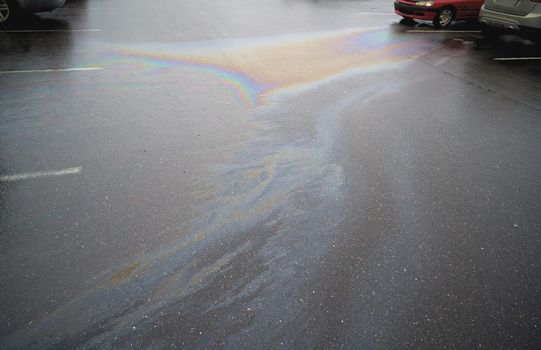 Colorful gas stain on wet asphalt. Oil stain caused by a leak under a car or truck.Environmental pollution concept.
