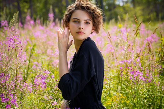 A young woman against the background of blooming Ivan-tea on a bright sunny summer day.The concept of youth