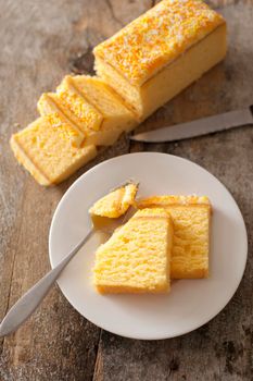 Fresh vanilla sponge cake with flavored icing sliced and served on a plate with a mouthful broken off on a fork and the remainder of the loaf alongside