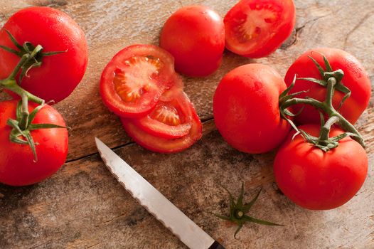 High-angle close-up view of fresh and juicy tomatoes as a nutritious ingredient next to a knife on a rustic wooden table