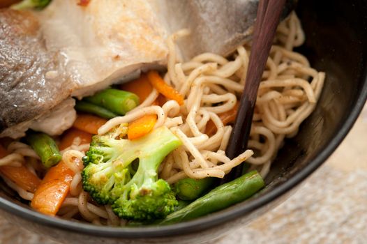 Healthy Asian fish and vegetable noodles in a close up view with broccoli and carrots served in a black bowl