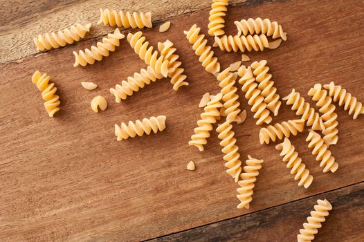 High-angle close-up view of raw Italian fusilli or spiral pasta scattered on a rustic brown wooden table