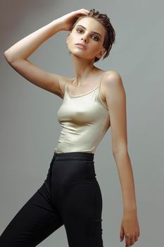 Attractive young woman in tight t-shirt and pants posing on a gray background