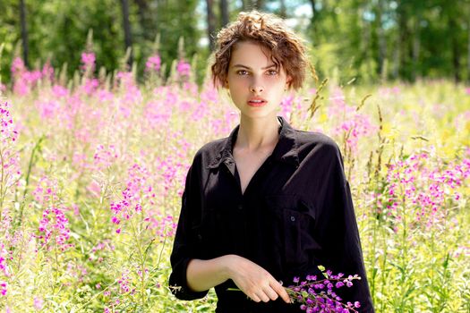 A young woman with a bouquet of lupines in her hand against the background of blooming Ivan-tea on a bright sunny summer day.Concept of youth