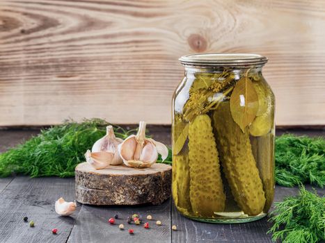Pickled cucumbers on wooden background. Pickles in glass jar with garlic, peppercorn and fresh dill. Salted cucumber in jar with copy space
