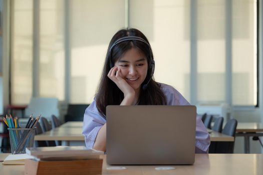 Portrait young asian girl looking camera while using laptop computer.