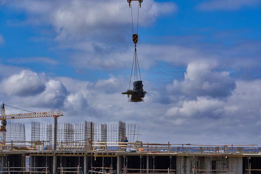 The load is suspended from the cable of a crane against the background of a cloudy sky and a house under construction