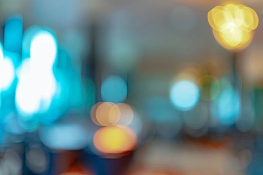 Blurred orange, yellow, and blue light bokeh abstract background. Defocused orange and white light on coffee shop or office interior. Bokeh background of modern light decoration in the building.