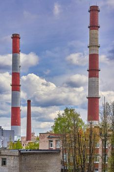 Tall factory chimneys against the backdrop of cloudy sky and residential buildings. Environmental pollution and urban ecology