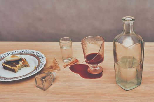 A broken glass and red tomato juice spilled on the table next to bottle of vodka. Concept drunkenness and alcoholism. Toning