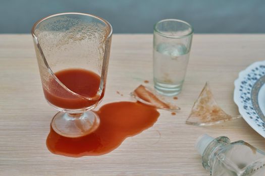 A broken glass and red tomato juice spilled on the table next to a bottle of vodka. Concept drunkenness and alcoholism