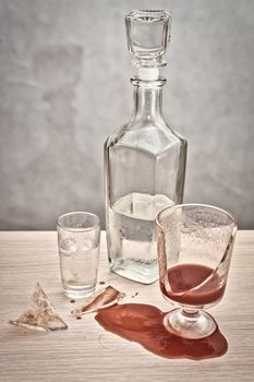 A broken glass and red tomato juice spilled on the table next to a bottle of vodka. Concept drunkenness and alcoholism