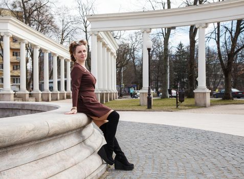 young woman posing sitting by a fountain on a city streeton spring day