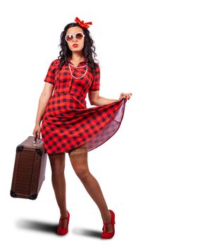 young woman pin-up style in red dress and sunglasses posing standing with suitcase in studio on white background
