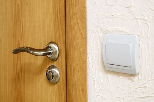 door handle on a wooden door near the wall with a switch indoor closeup