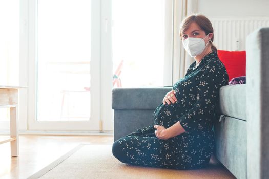 Pregnant woman with ffp2 face mask is sitting on the floor.