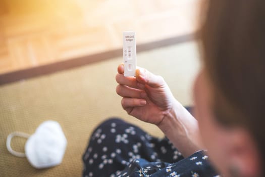 Close up of female fingers holding express antigen covid test, positive result, ffp2 mask in blurry background