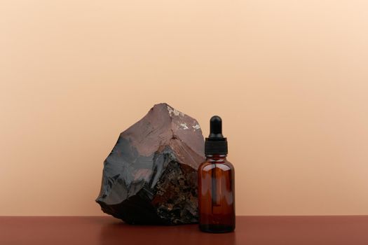 Skin serum in dark brown bottle with black cap next to dark stone against beige background with copy space. Concept of skin care and beauty. Anti aging and moisturizing skin serum for daily use