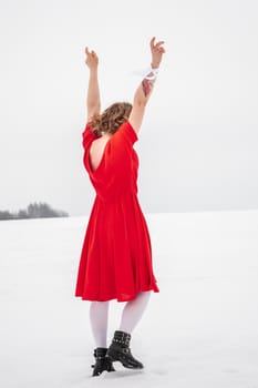 Beautiful woman in a red dress posing outside on a snowy field. She is wearing red dress and have tattoo on her arm.