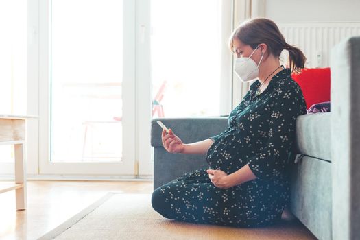 Pregnant woman with ffp2 face mask is sitting on the floor, holding express antigen covid test