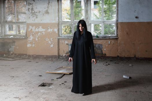 young goth woman in black dress standing in room of abandoned house