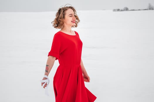 Beautiful woman in a red dress posing outside on a snowy field. She is wearing red dress and have tattoo on her arm.