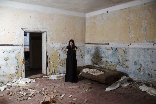 young goth woman in black dress standing in room of abandoned house