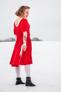 Beautiful woman in a red dress posing outside on a snowy field. She is wearing red dress and have tattoo on her arm.