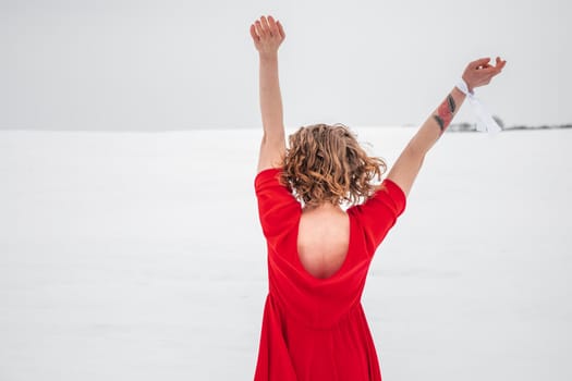 Beautiful woman in a red dress posing outside on a snowy field. She is wearing red dress and have tattoo on her arm.