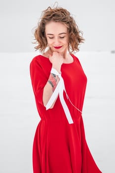 Beautiful woman in a red dress posing outside on a snowy field. She is wearing red dress and have tattoo on her arm.