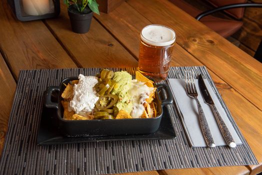 Nachos with glass of draft beer on wooden background.