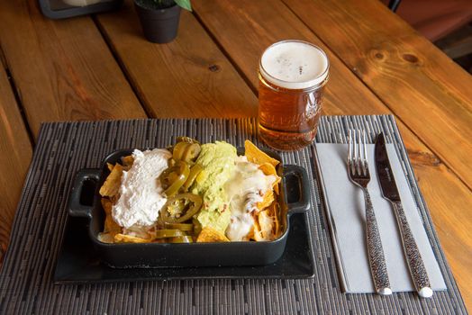 Nachos with glass of draft beer on wooden background.