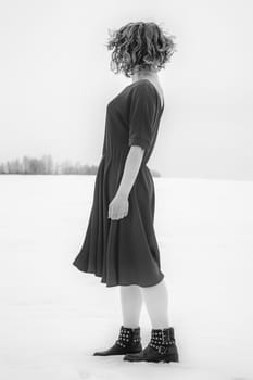 Beautiful woman in a red dress posing outside on a snowy field. She is wearing red dress and have tattoo on her arm.