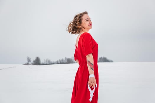 Beautiful woman in a red dress posing outside on a snowy field. She is wearing red dress and have tattoo on her arm.