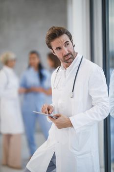 Shot of a mature doctor using digital tablet and pensive looking out the window while having quick break in a hospital hallway.