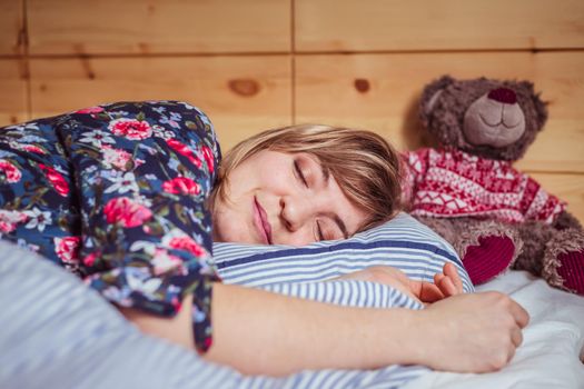 Young woman is sleeping peacefully with her teddy bear in her bedroom