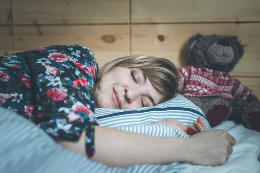 Young woman is sleeping peacefully with her teddy bear in her bedroom